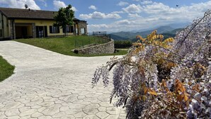 A paved pathway leading to a yellow building with a stone wall and a view of mountains in the background. - Villa Cavalieri in Vedriano with a panoramic view of the Reggio Emilia hills (Canossa)