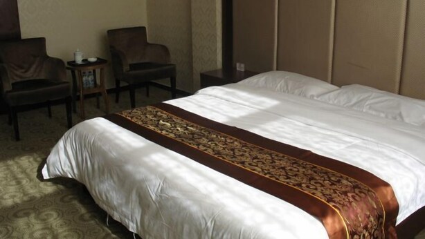 A hotel room with a large bed, two chairs, a small table, and a headboard. - Lidu International Hotel (Ar Horqin Banner)
