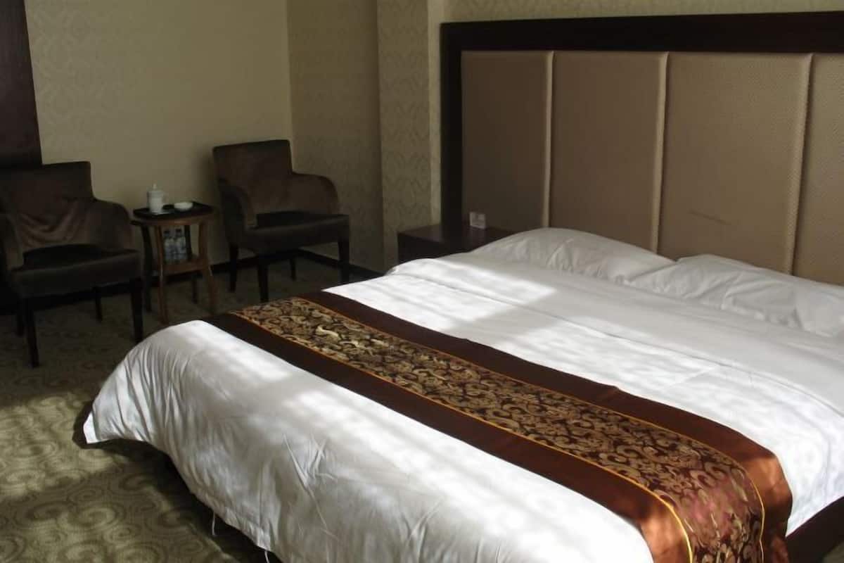 Ein Hotelzimmer mit einem großen Bett, zwei Stühlen, einem kleinen Tisch und einem Kopfteil.