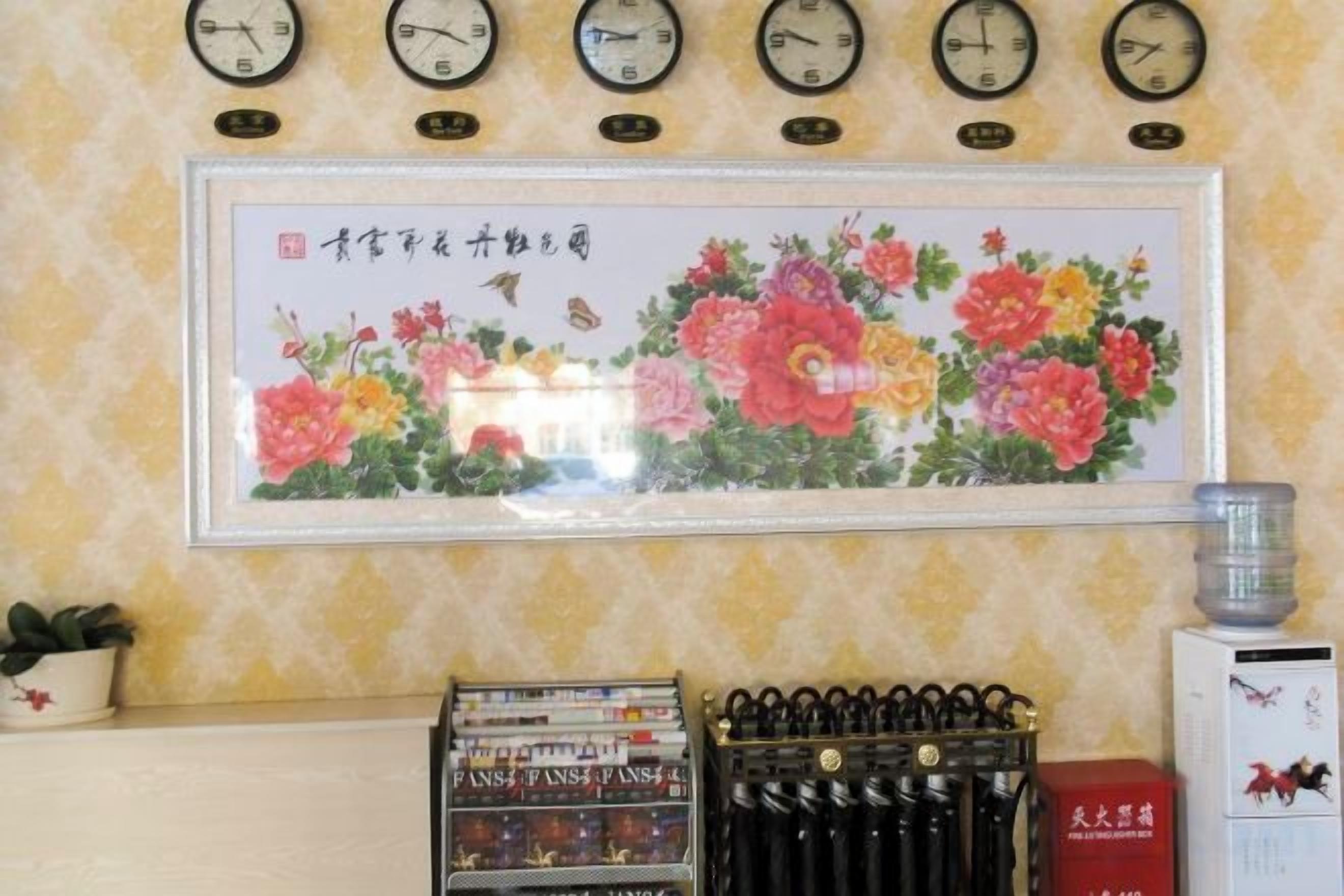 A wall with clocks, a framed floral painting, and a water dispenser.