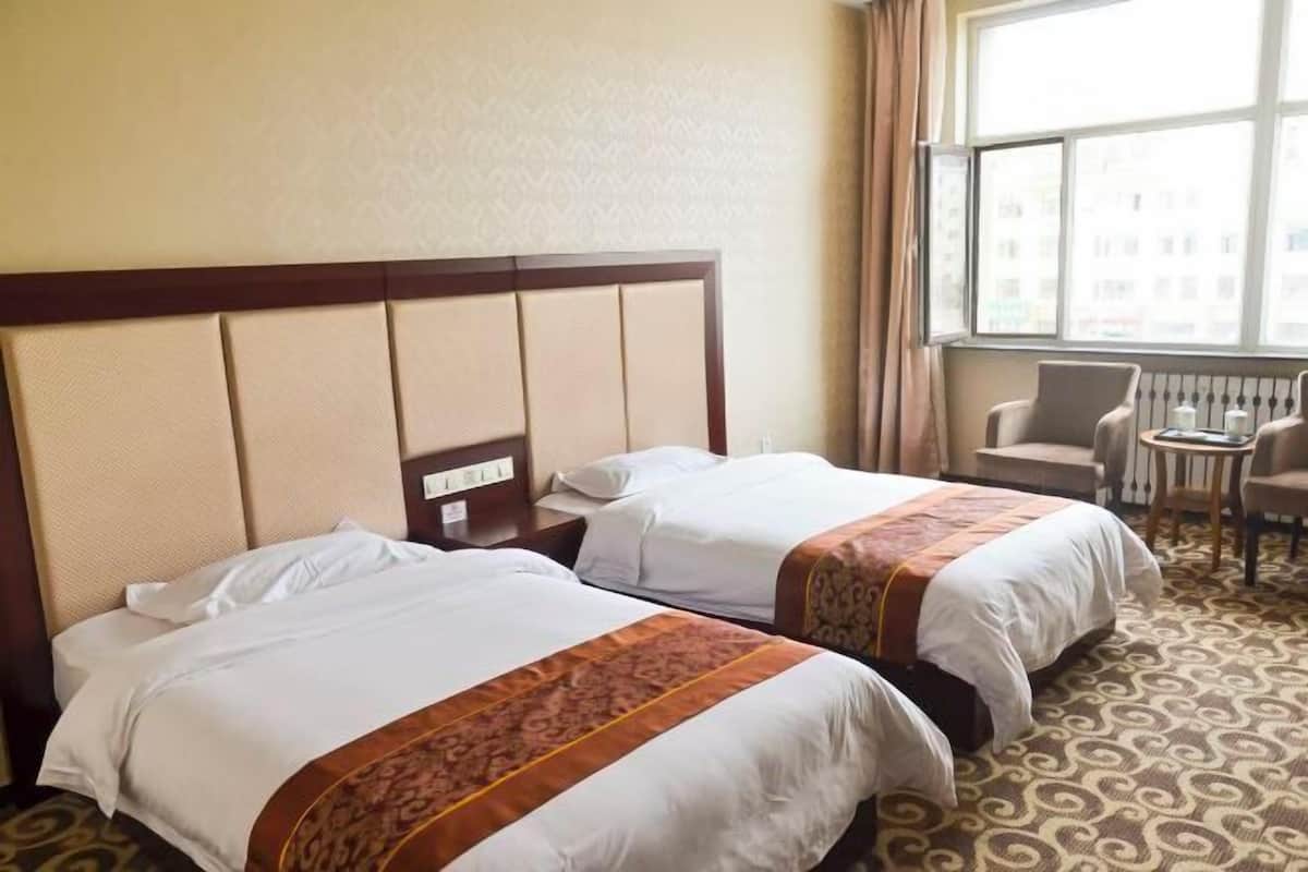 Ein Hotelzimmer mit zwei Betten, einem Fenster mit Blick, einem kleinen Tisch und einem Sessel.