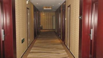 A hotel corridor with doors on both sides, carpeted floor, and a ceiling light fixture.