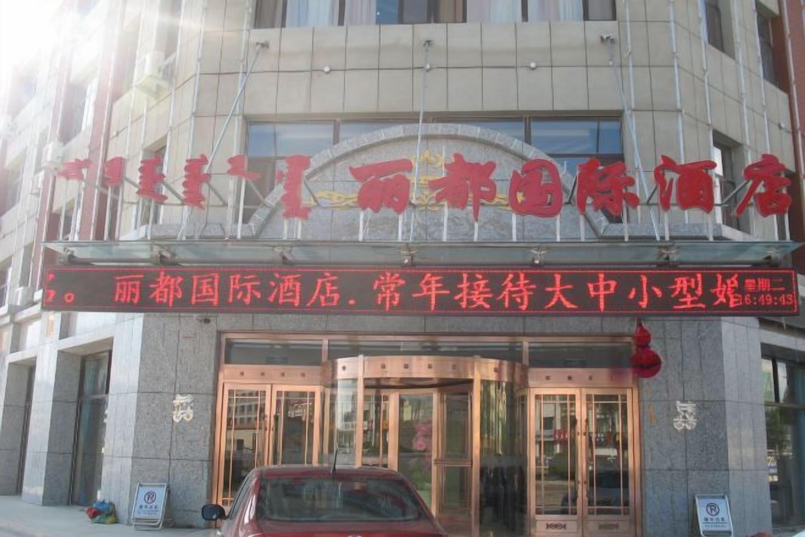 A hotel entrance with a signboard, glass doors, and a red car parked outside.