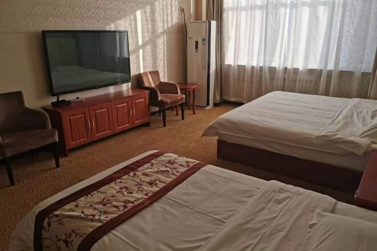 Ein Hotelzimmer mit Fernseher, Schreibtisch, zwei Betten und einem Sessel.