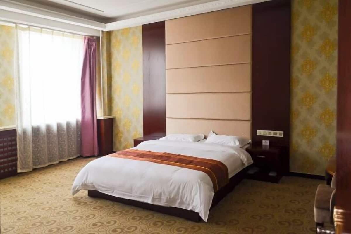 Ein Hotelzimmer mit einem großen Bett, einem Nachttisch, einem Holzkopfende und einem gemusterten Teppich.