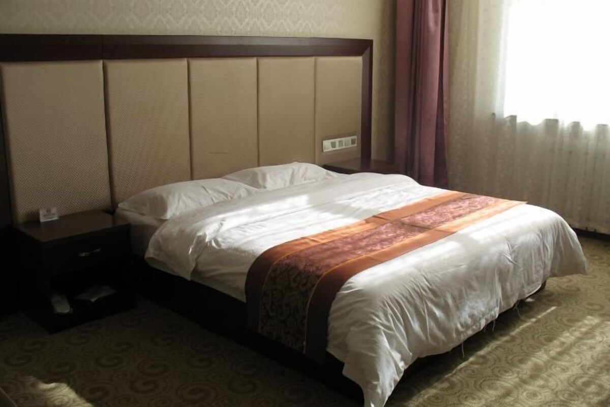 Une chambre d’hôtel avec un grand lit, une table de chevet et une fenêtre avec des rideaux.