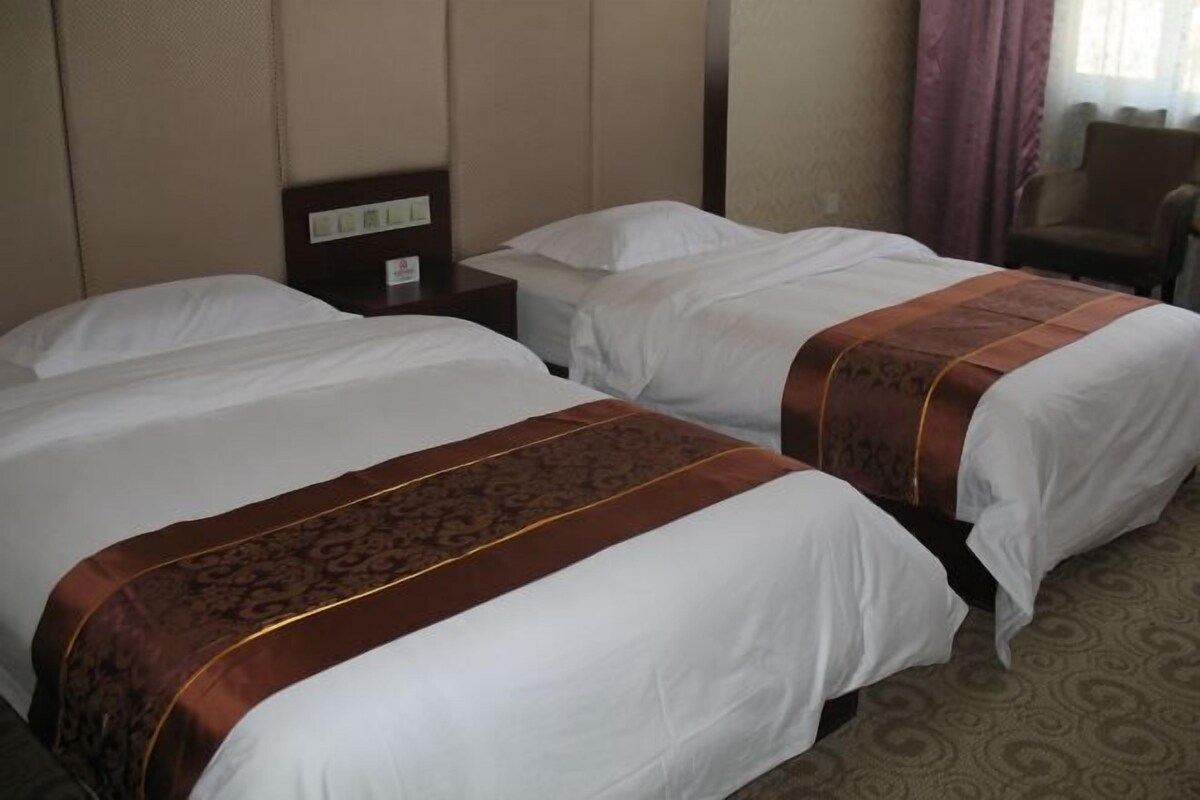 Une chambre d’hôtel avec deux lits, une table de chevet, une chaise et une fenêtre avec des rideaux.