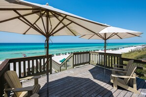 A wooden deck with beach umbrellas and chairs overlooking a beach with white sand and turquoise water.