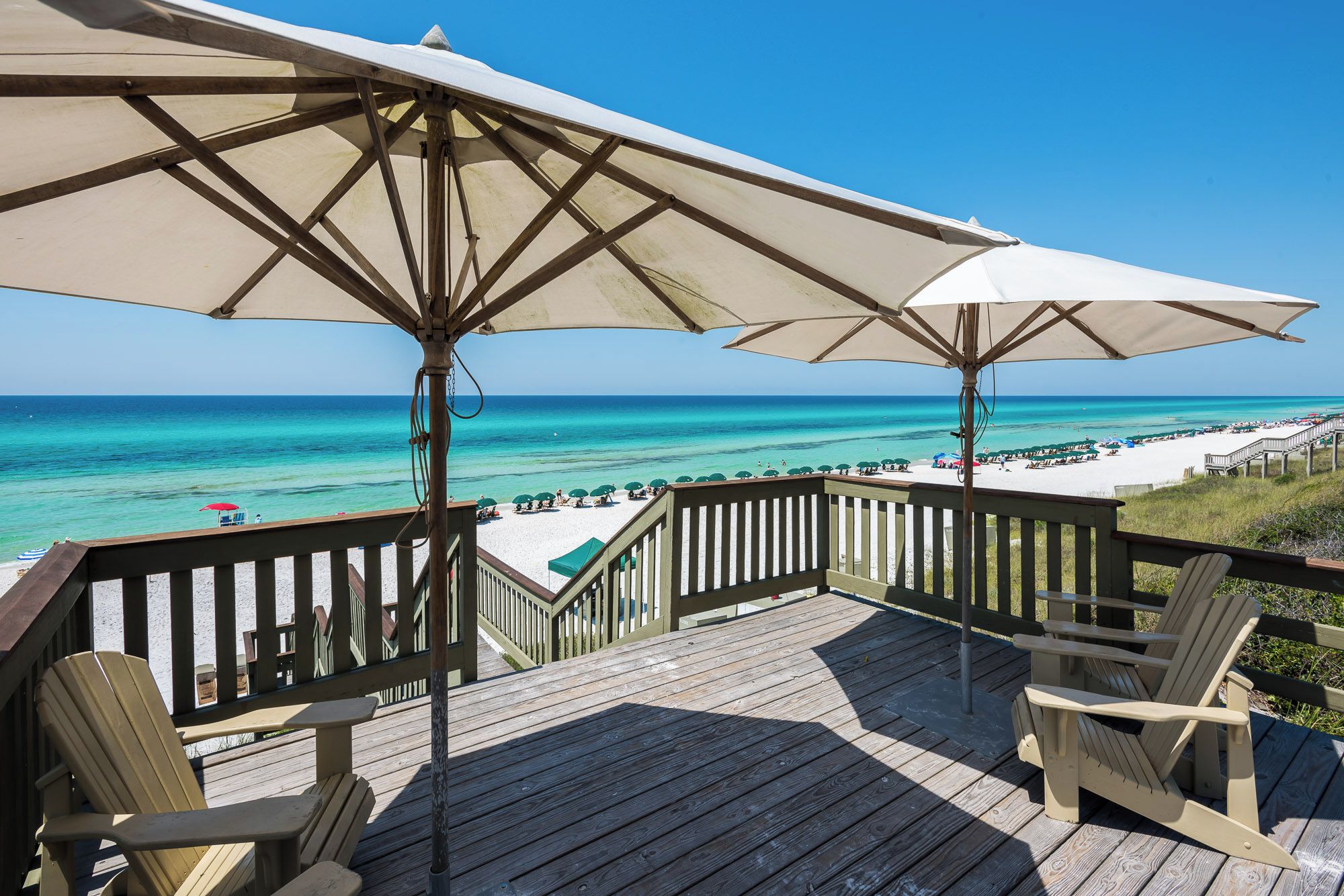 Une terrasse en bois avec deux grands parasols, une vue sur la plage et une chaise.