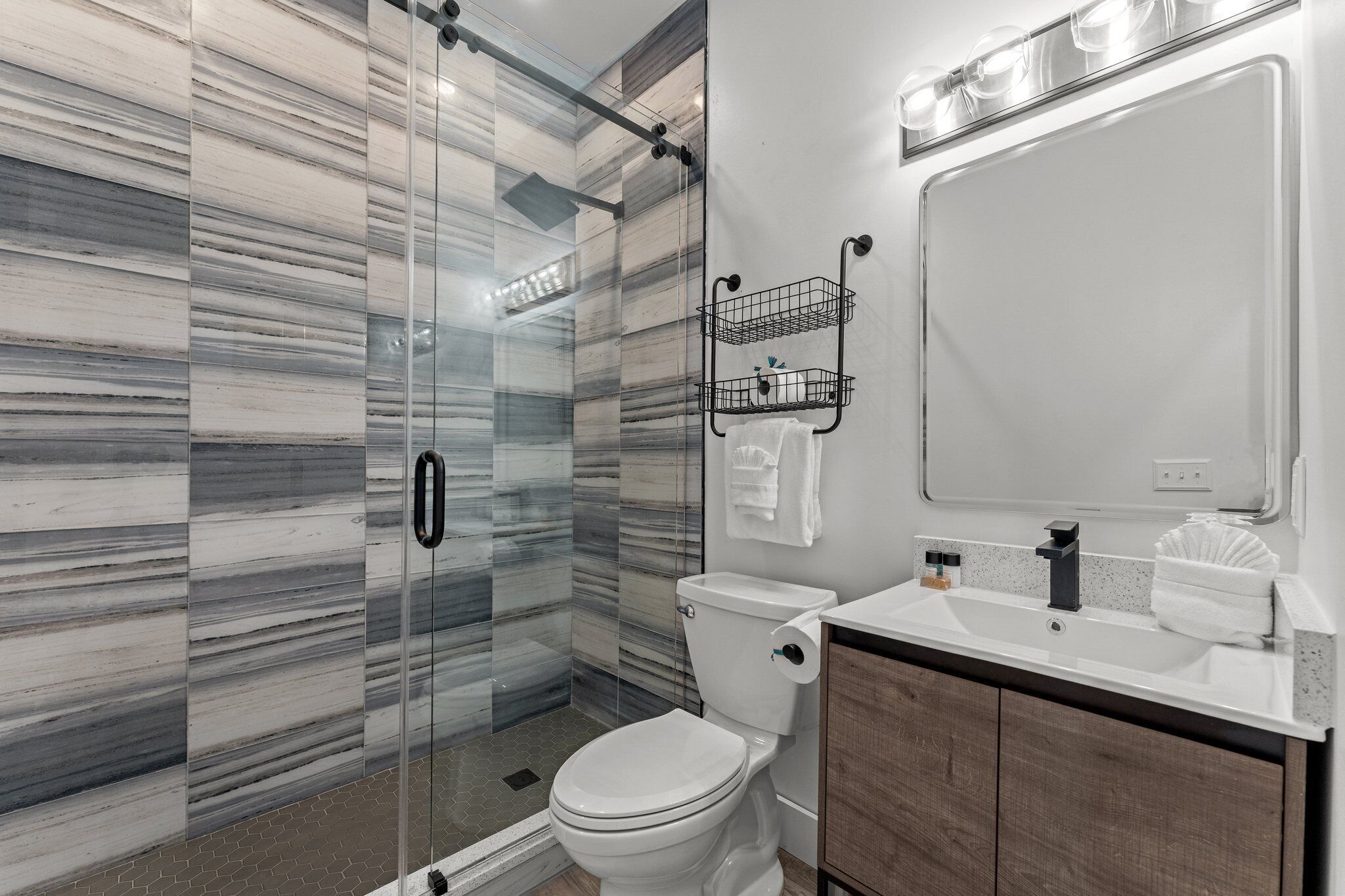 Une salle de bain moderne avec une douche à parois de verre, des toilettes blanches, un lavabo avec un miroir et un porte-serviettes.