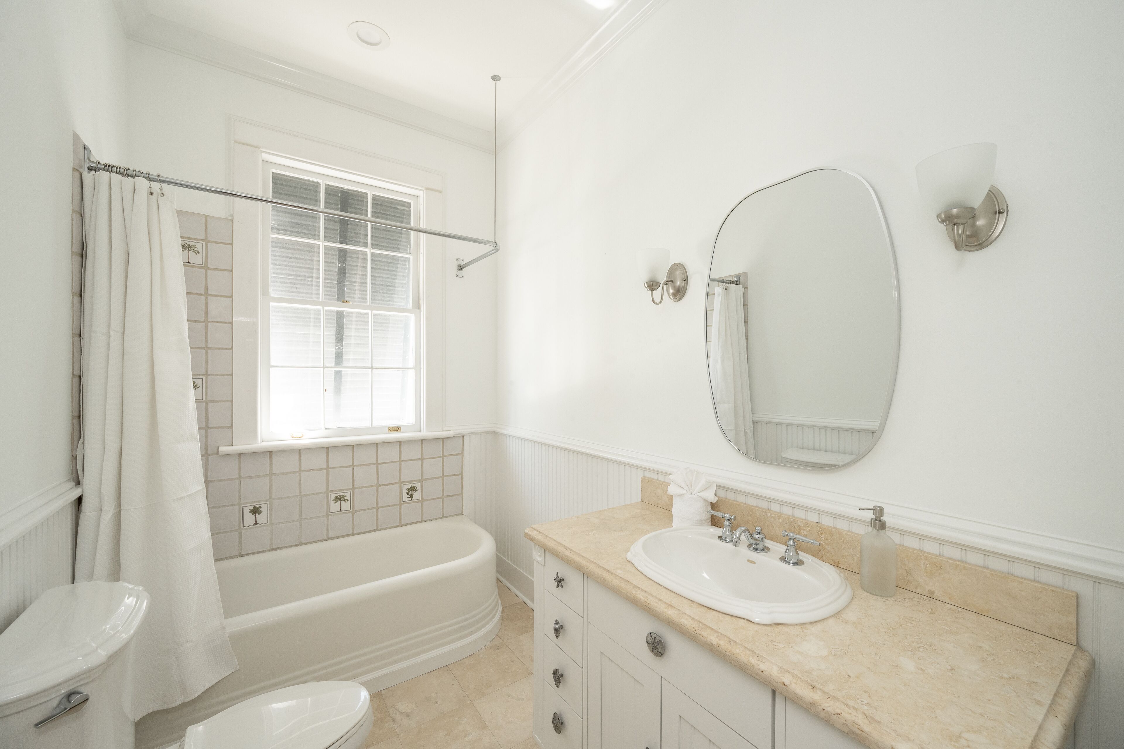 Ein Badezimmer mit Badewanne, Toilette, Waschbecken und einem Fenster mit Duschvorhang.