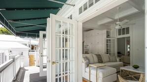 Een ruim balkon met een witte reling, een witte deur met ruitpanelen en een witte bank met kussens.