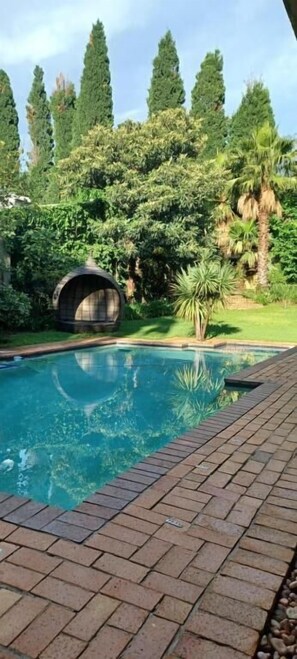 Une piscine bordée de briques, entourée d’une végétation luxuriante et de grands arbres.