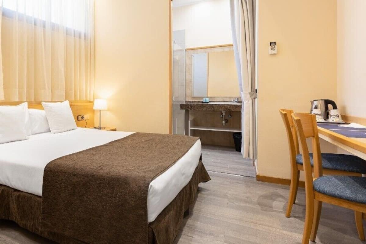 A hotel room with a bed, bedside tables, a desk with a chair, and a bathroom visible through an open door.