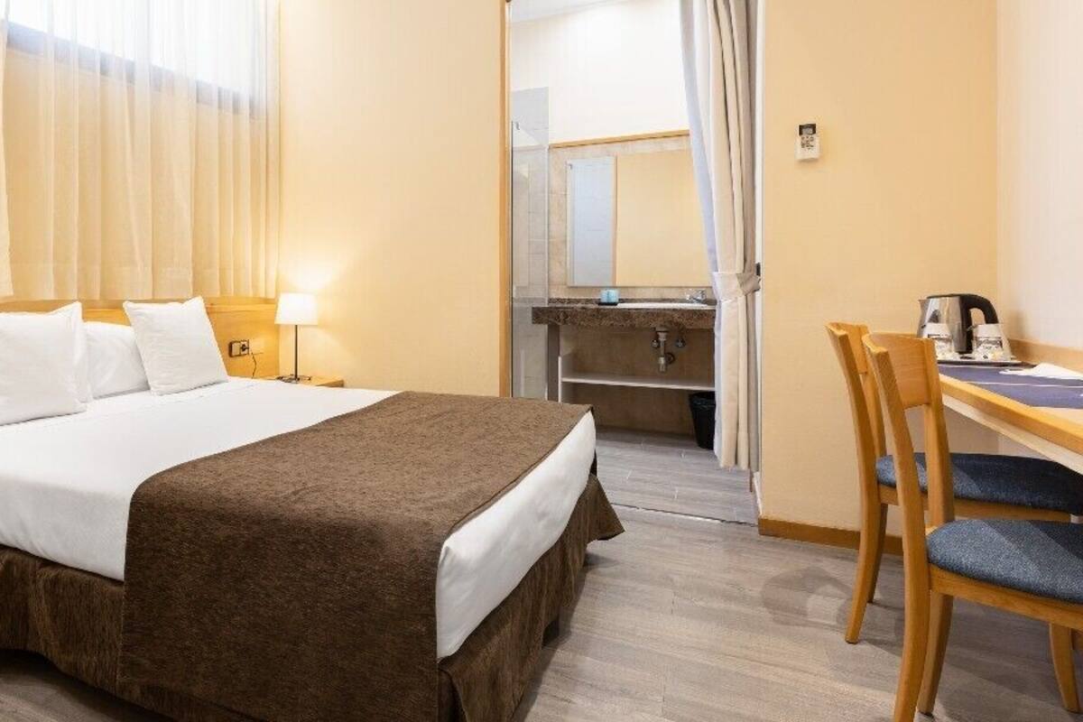 A hotel room with a bed, bedside tables, a desk, and a chair.