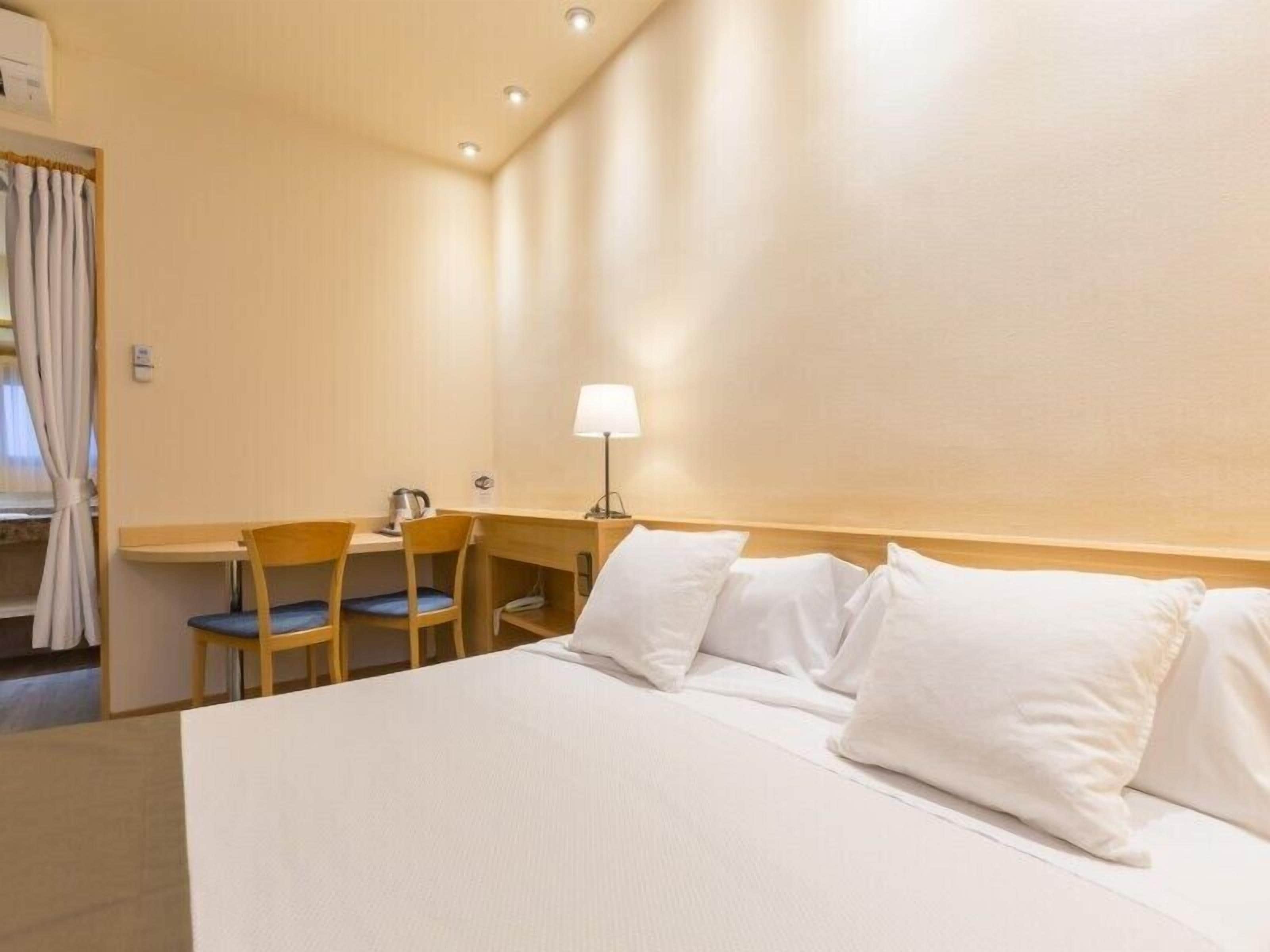 Hotelkamer met een bed, bureau, stoel, lamp en raam met gordijnen.