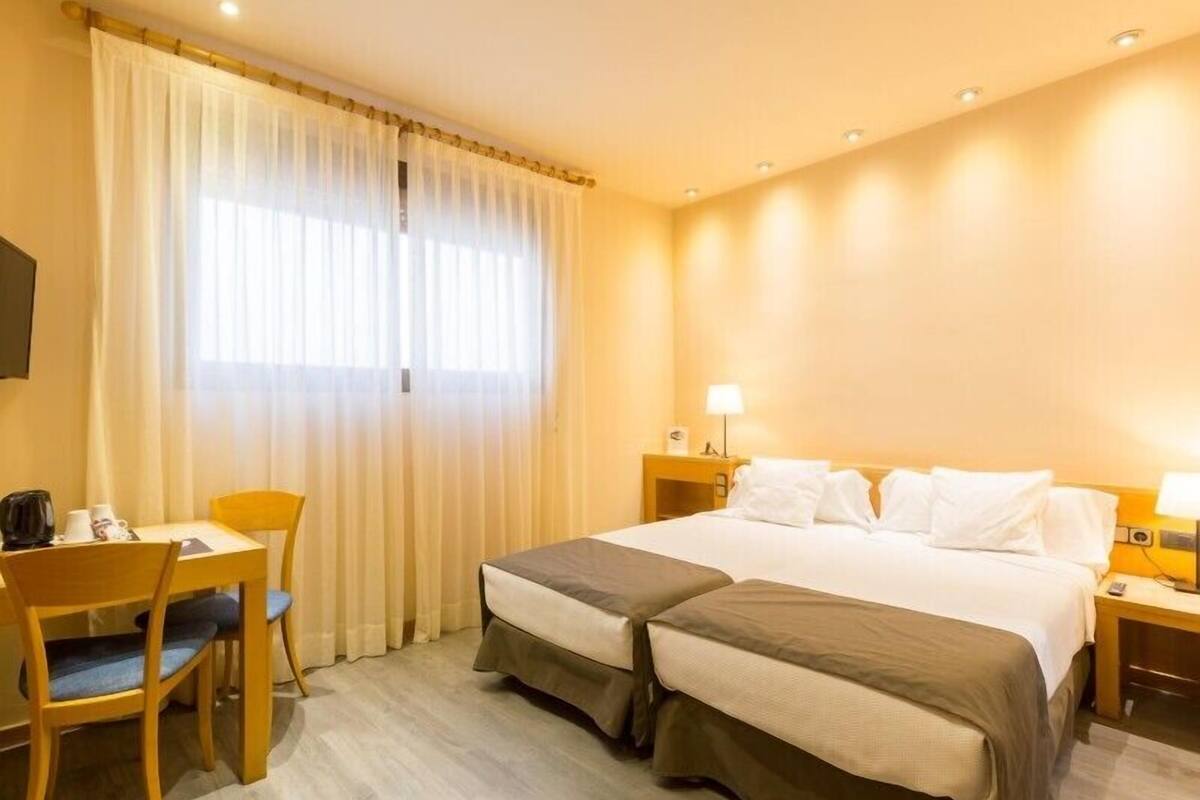 A hotel room with a bed, two bedside tables, a chair, a desk, and a window with curtains.