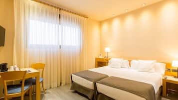 Une chambre d’hôtel avec un lit, deux tables de chevet, une chaise, un bureau et une fenêtre avec des rideaux.
