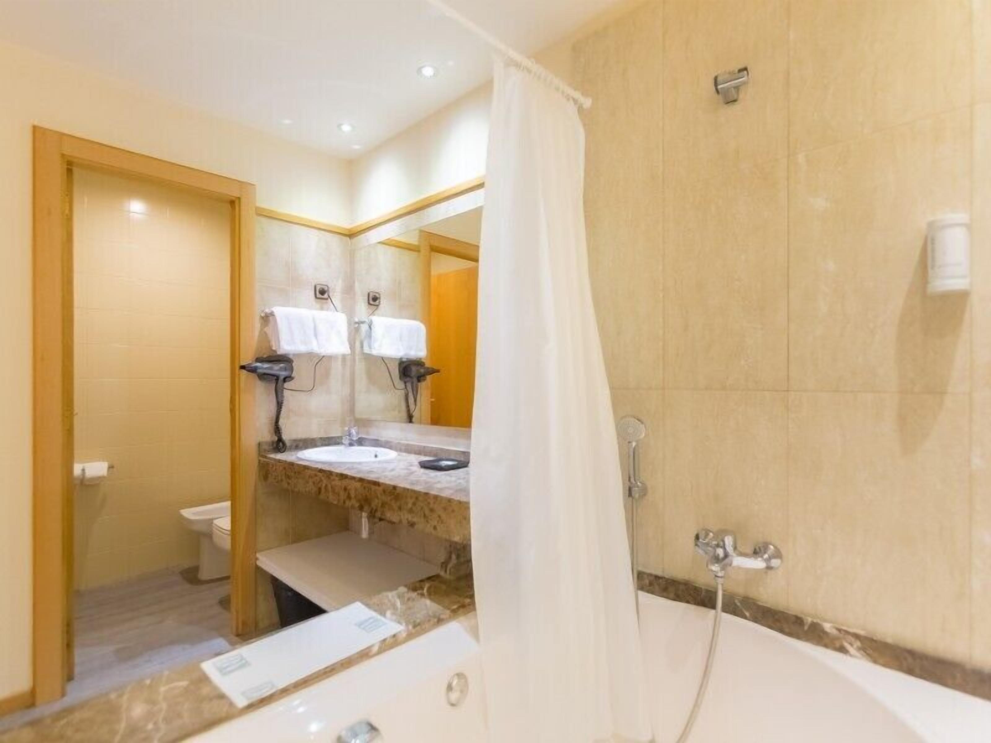 A bathroom with a bathtub, a sink, and a toilet. There are two towel racks with white towels hanging.