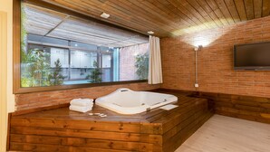 A modern room with a wooden floor, a large window, a wooden bench, and a flat-screen TV mounted on the wall. - Hospedium Apartamentos DV (Barcelona)
