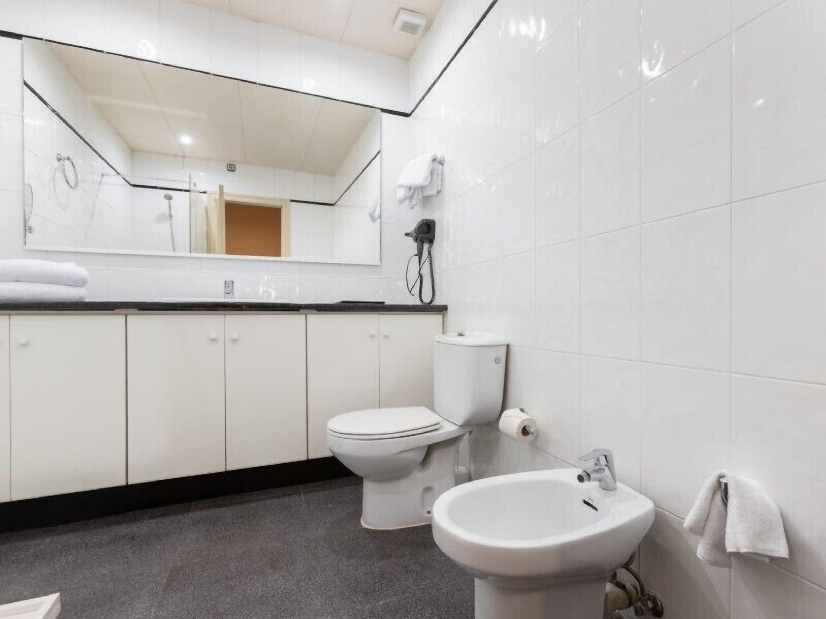 Un baño moderno con inodoro, bidé y lavamanos, todo en color blanco.