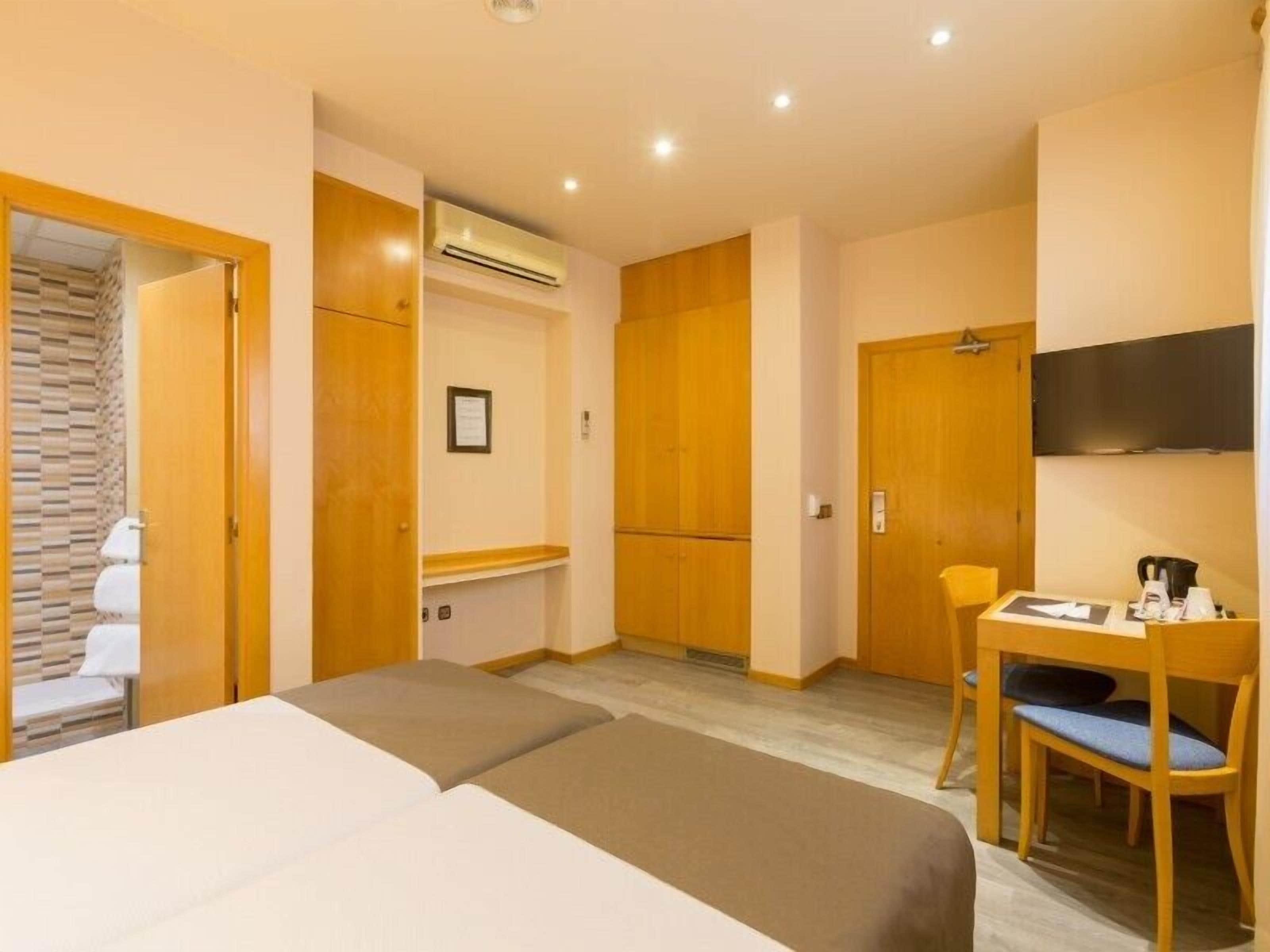 Une chambre d’hôtel avec deux lits, un bureau avec une chaise, une télévision et un appareil de climatisation.