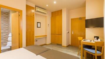 Una habitación de hotel con dos camas, un escritorio con silla, televisor y unidad de aire acondicionado.