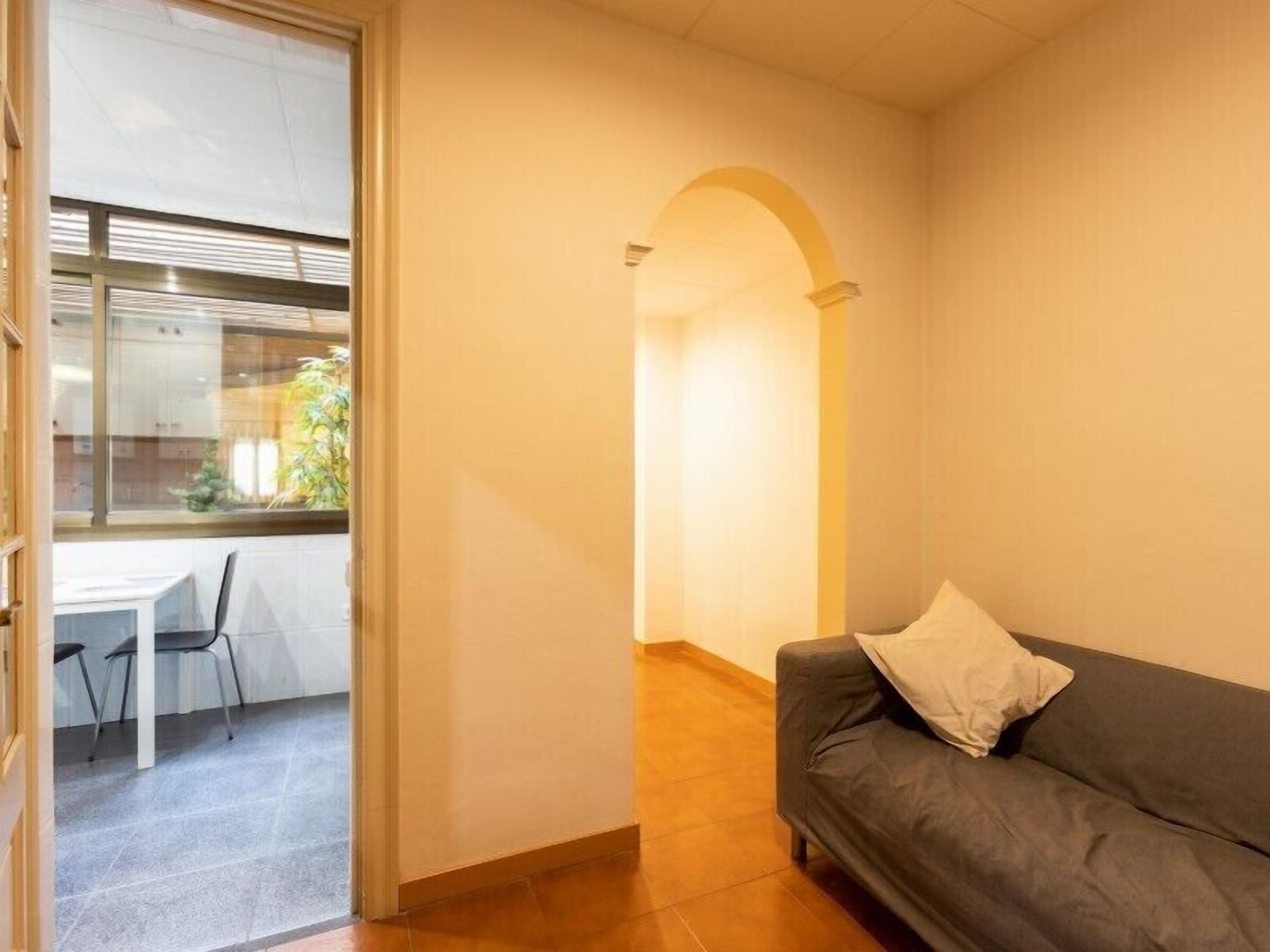 Una habitación con un sofá gris, una mesita con sillas y una ventana con persianas.