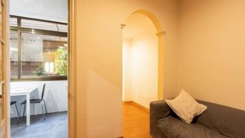 Una habitación con un sofá gris, una mesita con sillas y una ventana con persianas.