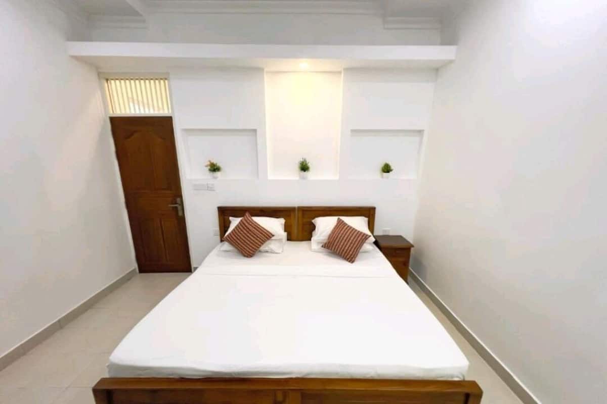 A bedroom with a wooden bed, white bedding, two bedside tables, and a wall-mounted light fixture.