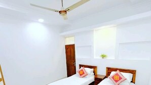 A clean, well-lit room with two wooden beds, a ceiling fan, and a small window. - Everest Lodge  (Hulhudhoo)