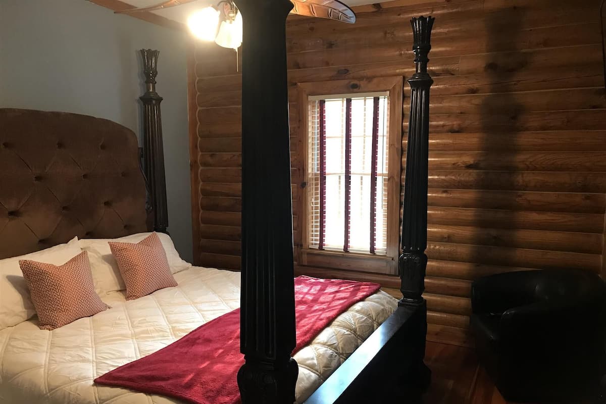 Uma cama de dossel com cabeceira acolchoada e manta vermelha.