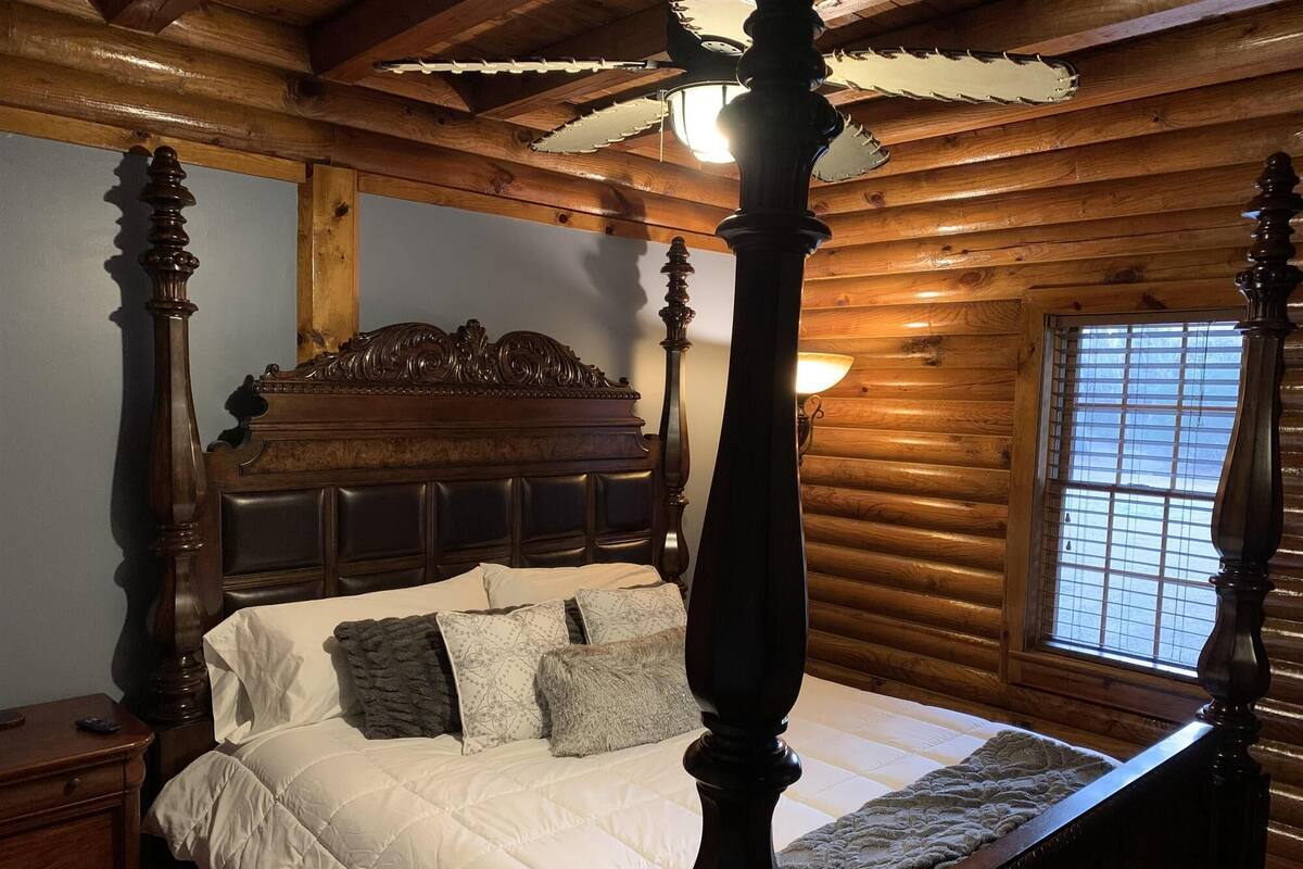 Uma cama de dossel com cabeceira de madeira, colcha branca e várias almofadas.