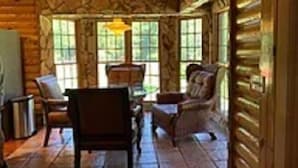 A log cabin interior with a stone fireplace, wooden furniture, and large windows. - Beachwoods Inn (Loris)