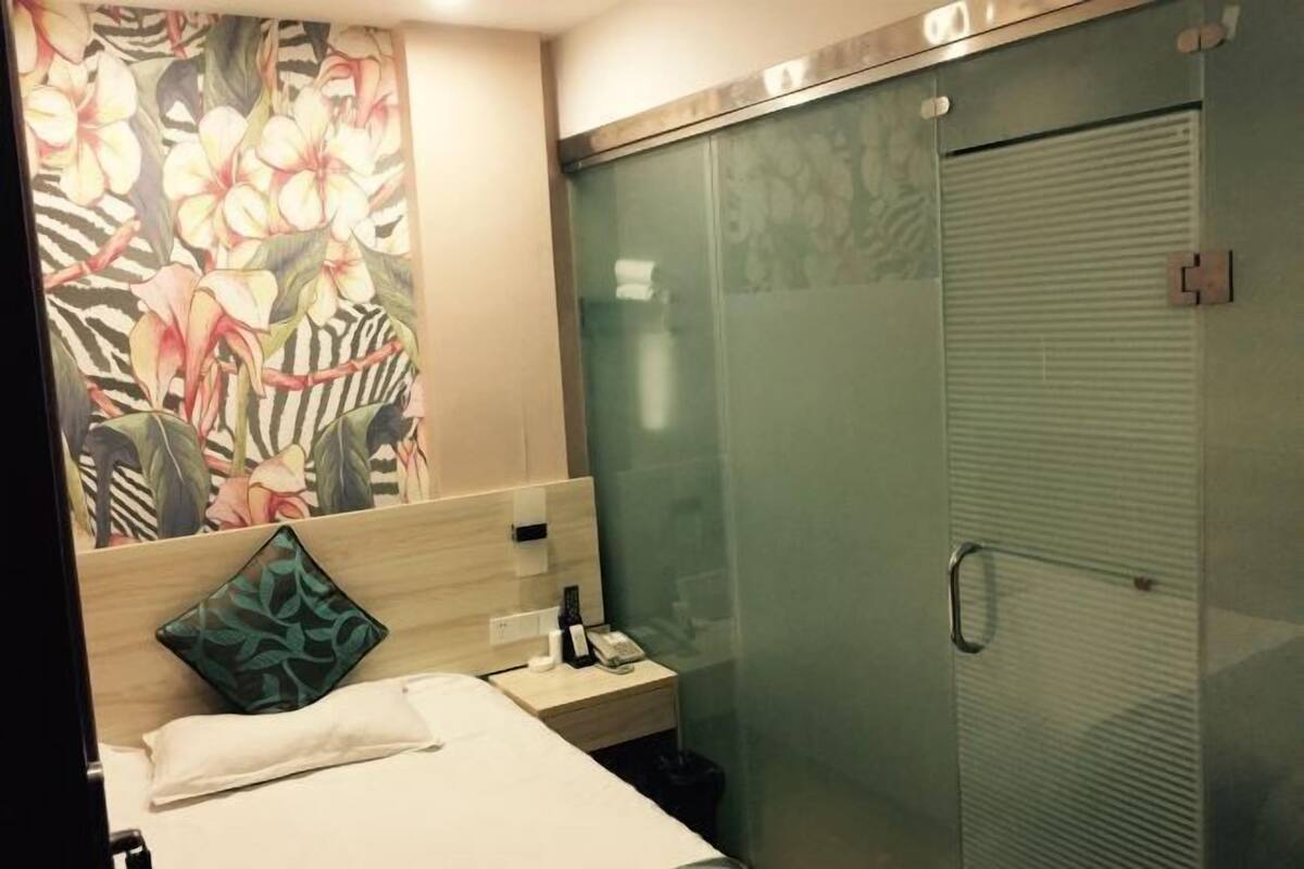 A hotel room with a bed, a nightstand, a telephone, and a glass-enclosed shower area.