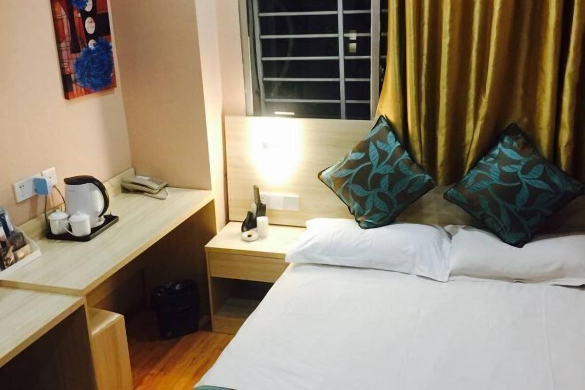 A hotel room with a bed, a desk with a telephone, a coffee maker, and a window with curtains.