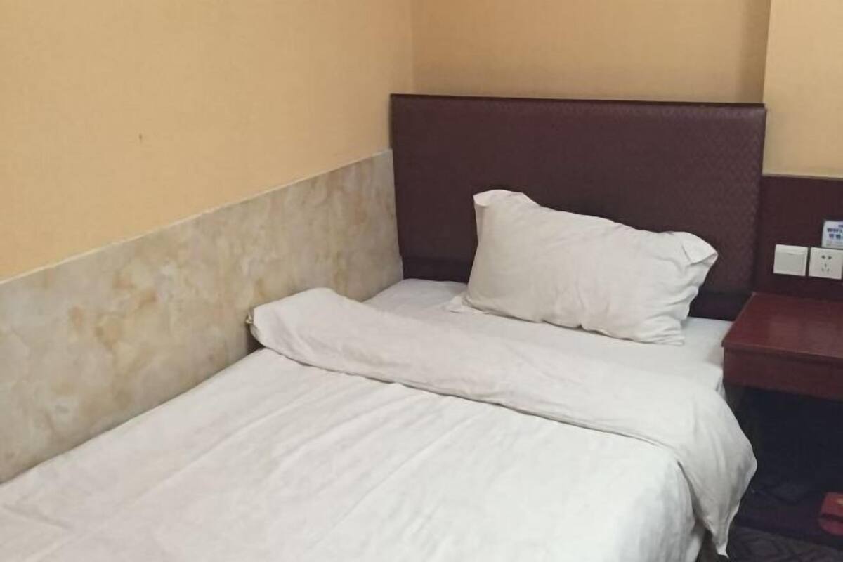 A single bed with a headboard, a bedside table, and a wall socket.