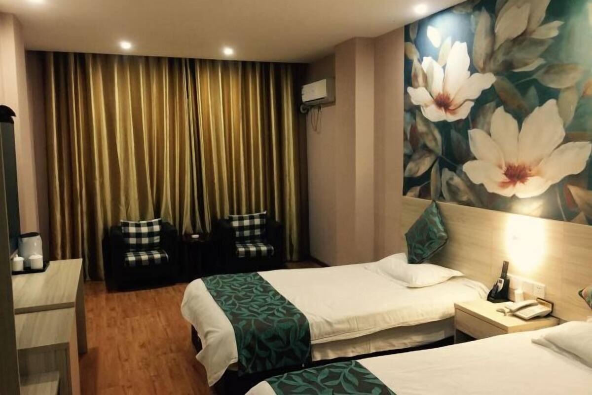 A hotel room with two beds, a desk, a chair, a wall-mounted air conditioner, and a floral mural.