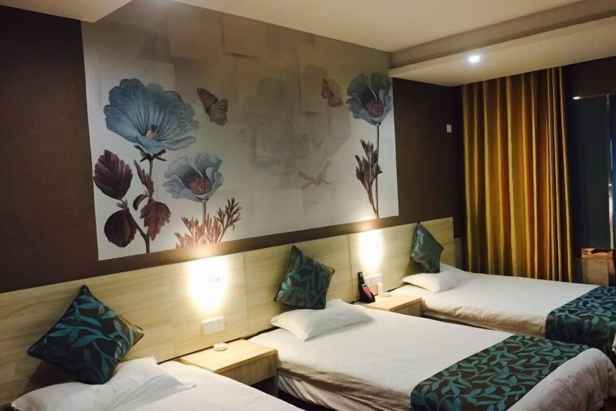 A hotel room with two beds, a large floral mural on the wall, and a curtain on the window.