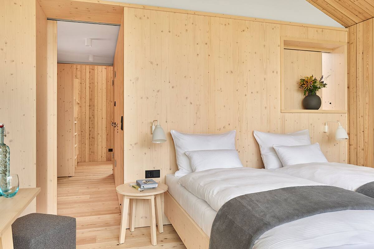 Une pièce en bois avec un lit, une table de chevet, une lampe et une petite table sur laquelle se trouvent une bouteille et un verre.