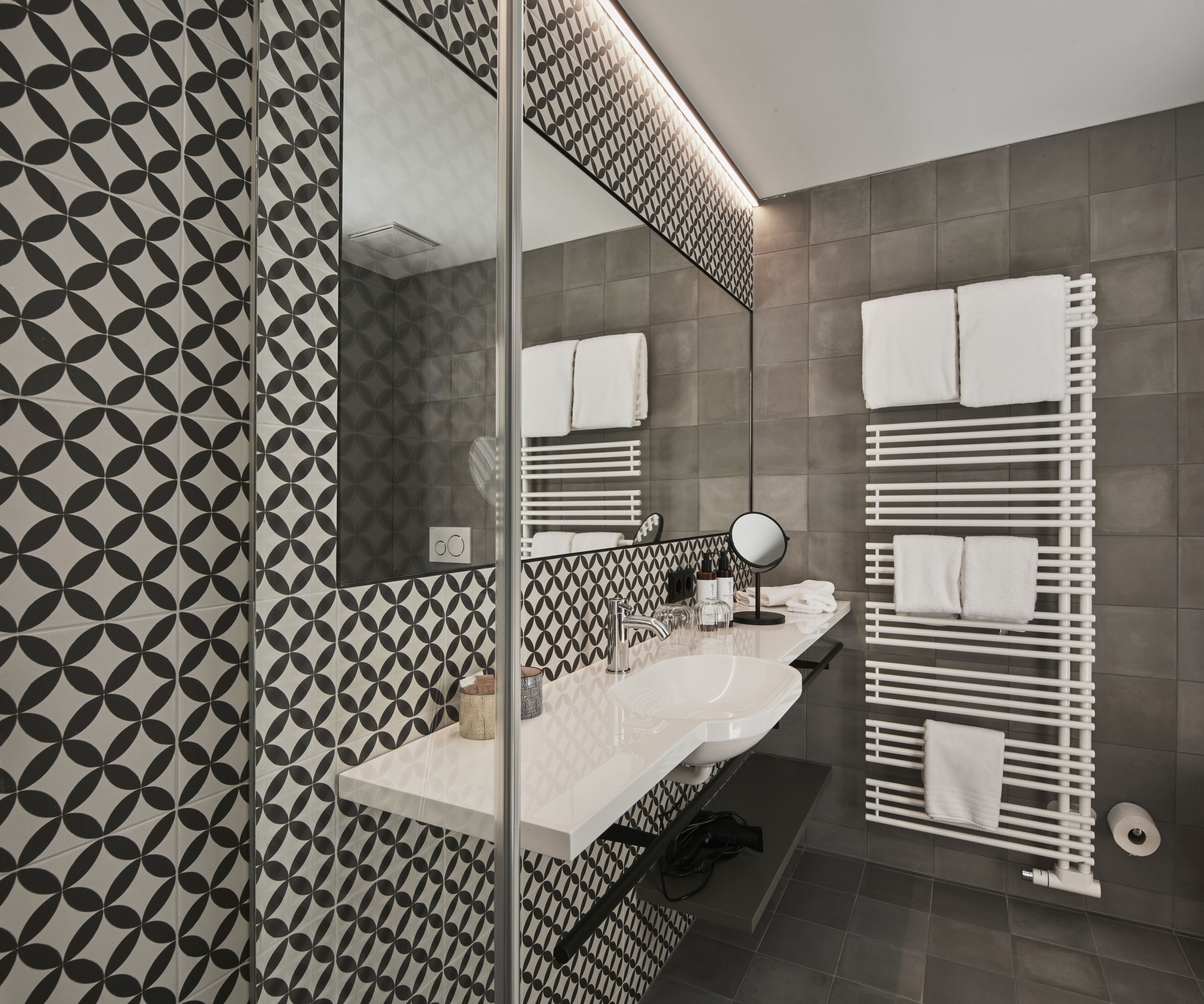 A modern bathroom with a geometric patterned wall, a white sink, a mirror, and a towel rack.