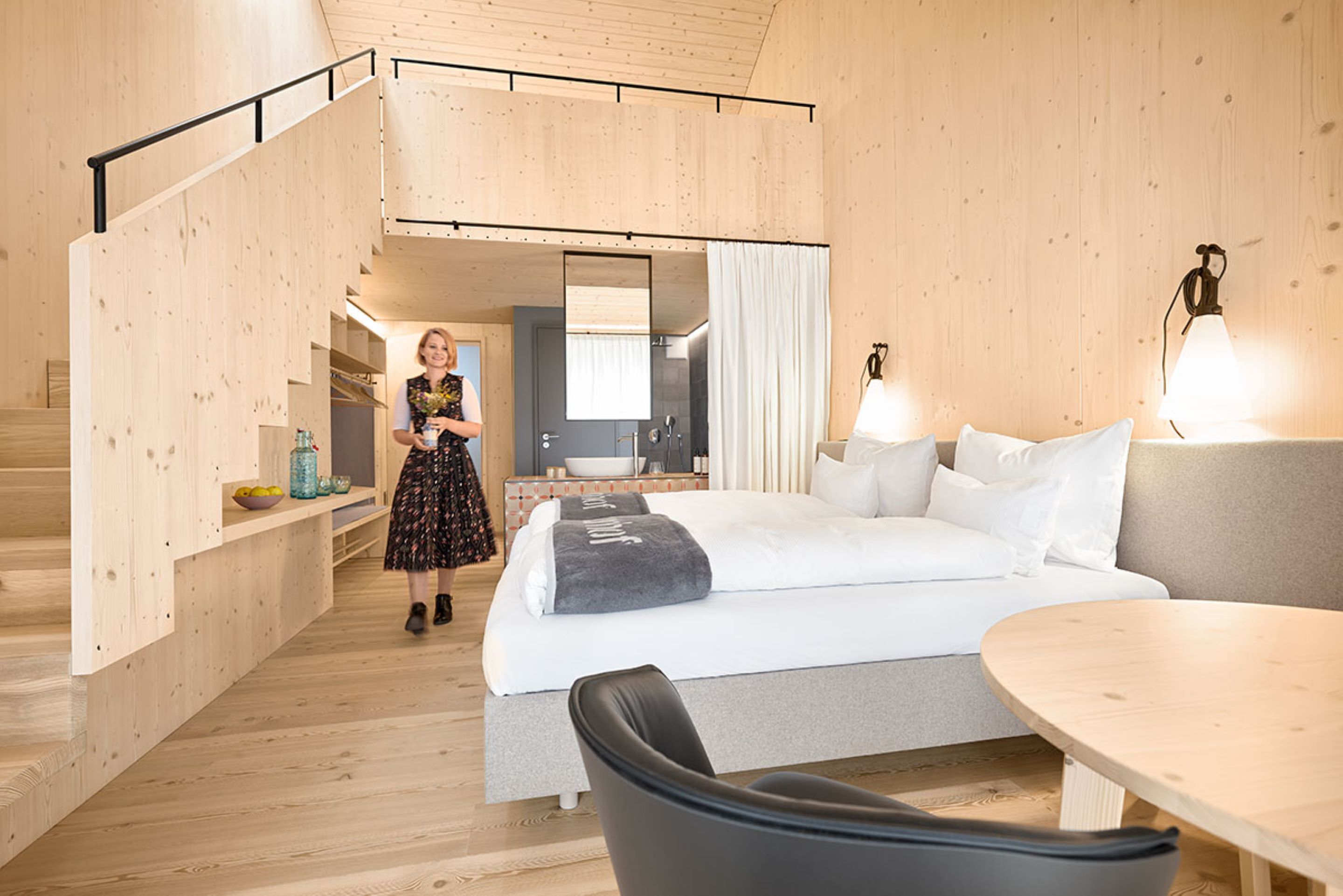 A modern hotel room with a wooden interior, a bed, a desk, and a staircase.