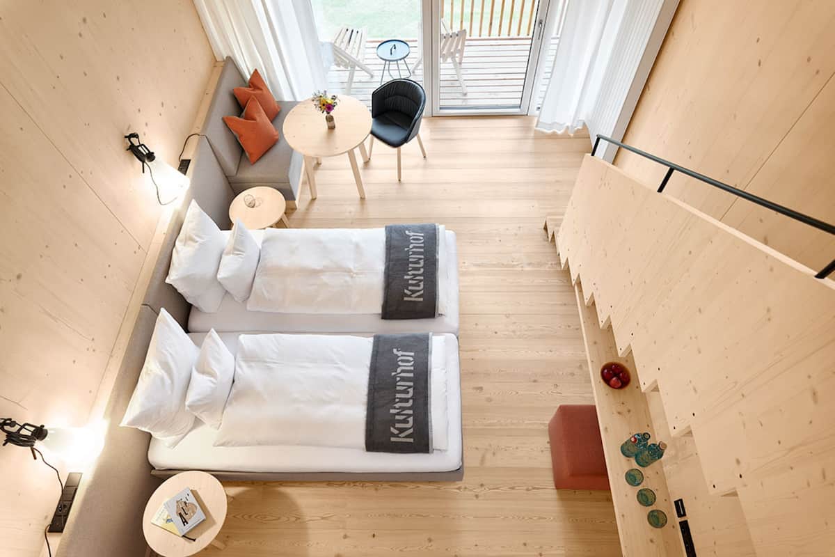 Une chambre moderne avec deux lits, une petite table ornée d’un vase, une chaise et une vue sur l’extérieur.