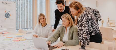 A group of people in a modern office with a large poster on the wall, a laptop, and sticky notes on the table.
