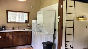A compact kitchen with wooden cabinets, a white refrigerator, a washing machine, and a black trash bin.