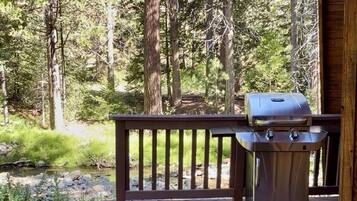 A wooden deck with a barbecue grill and a table with a plate of food and a mug.