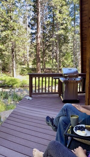A wooden deck with a barbecue grill and a table with a plate of food and a mug.