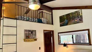 A room with a bunk bed, a ladder, a picture of a forest, a window with a view, and a door.