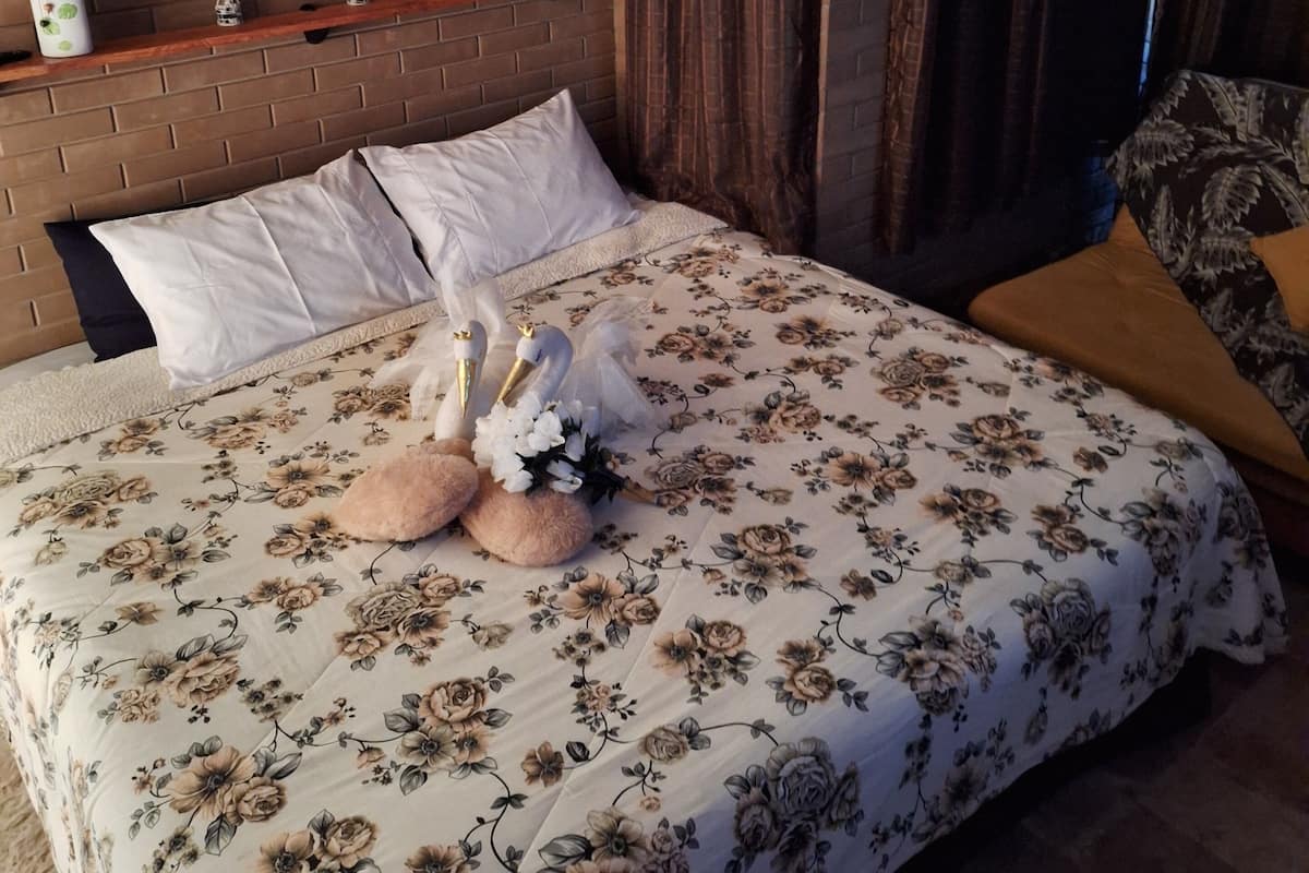 Ein Schlafzimmer mit einer blumigen Bettdecke, einem Ziegelkopfstück, einem Holzregal mit Dekorationen und einem Gemälde von Kirschblüten.
