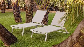 Two white lounge chairs with metal frames, positioned on a well-maintained grassy area with palm trees in the background.
